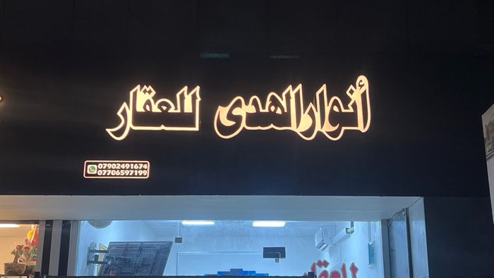واجهة مكتب عقاري ليلاً بحروف مضيئة تكتب أنوار الهدى للعقار
