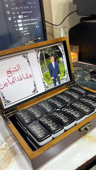 علبة خشبية مفتوحة تحتوي قطع دومينو سوداء مطبوع عليها اسم بالعربية