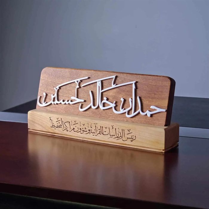 ستاند مكتبي خشبي عليه اسم بحروف عربية بيضاء بارزة ونقش للمنصب